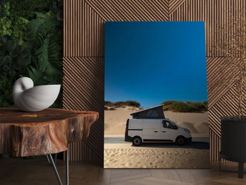 White camper van with pop roof parked near sand dunes in Tarifa, Cadiz, Spain. Vertical orientation with large blue sky copy space for text, concept of vanlife, road trip, and travel.