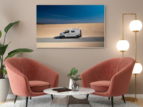 White camper van driving along a road through sand dunes in Tarifa, Cadiz, Spain. Wide panoramic view with copy space, concept of vanlife, road trip, and travel freedom.