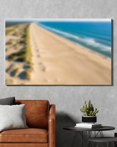 Aerial drone view of a vast, empty sandy beach with gentle ocean waves and a clear blue sky.