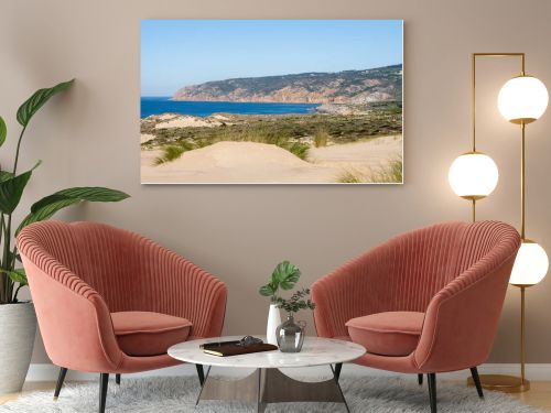 Sandy dune landscape with a wooden coastal path and distant rocky cliffs along the Atlantic coast near Guincho Cascais Portugal.
