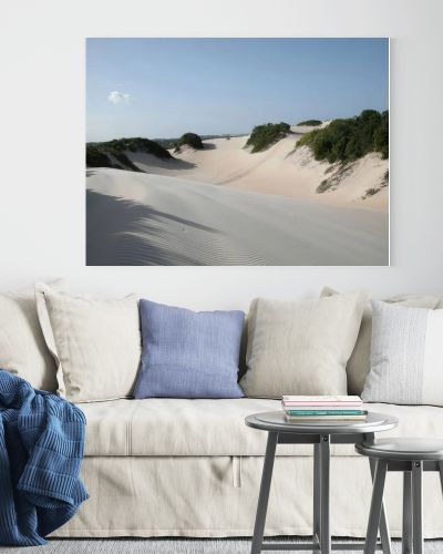 Expansive sand dunes with sparse green vegetation under a bright, clear blue sky, suggesting a coastal or desert landscape.