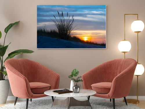 Evening sunset behind dune grass on Sylt after a passing rain shower, with warm orange light breaking through layered clouds above the North Sea coast