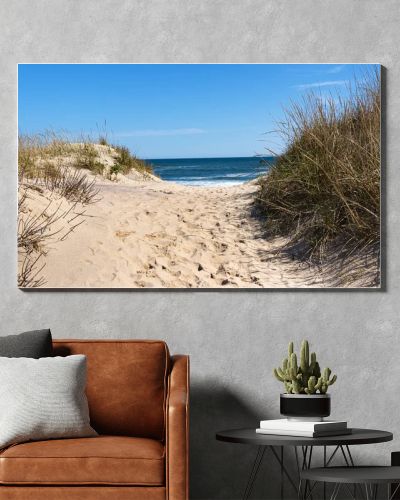 View of the Atlantic Ocean looking through a sand dune at Montauk Beach with footprints in the center and beach grass on the sides.