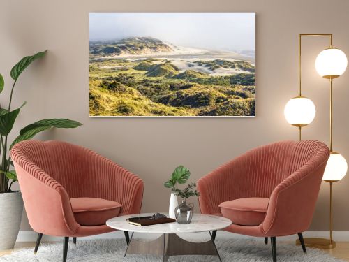 This breathtaking coastal landscape captures golden grassy sand dunes under bright sunlight, rolling toward a mist-covered beach. The scene blends textures of sand, grass, and ocean waves for a serene, natural beauty.