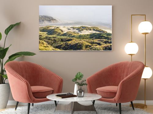 This breathtaking coastal landscape captures golden grassy sand dunes under bright sunlight, rolling toward a mist-covered beach. The scene blends textures of sand, grass, and ocean waves for a serene, natural beauty.