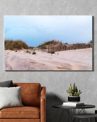 A sandy dune landscape with wooden fences lines the edge of a beach under an overcast sky. The scene captures the raw beauty of a coastal environment with a serene and untouched atmosphere.