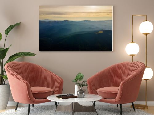 Aerial view of dark mountain hills with bright sunrays of setting sun at sunset. Hazy peaks and misty valleys in evening.