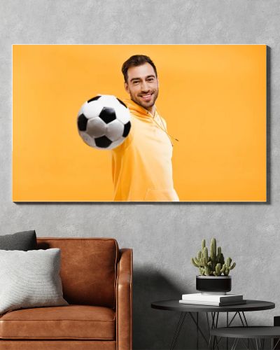 smiling man playing with football isolated on yellow