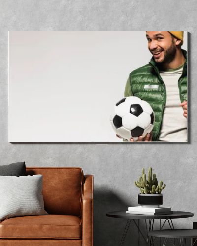 Smiling sportsman with football pointing with finger at camera isolated on grey, banner 