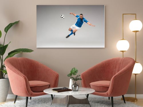 Sportsman looking at camera while jumping near football on grey background