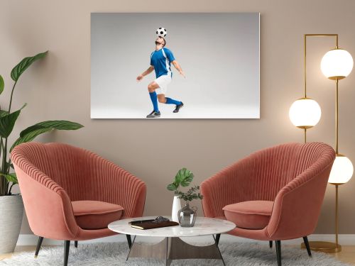 Sportsman holding football on head while balancing on grey background 