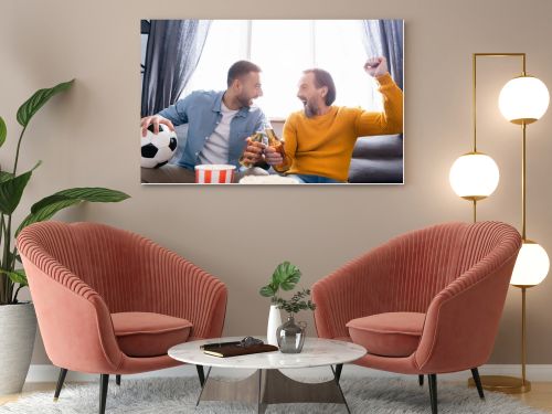 excited interracial dad and son clinking bottles of beer while watching football championship at home