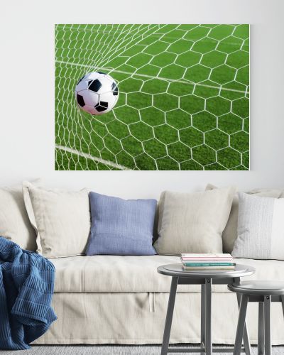 Soccer football in Goal net with green grass field.