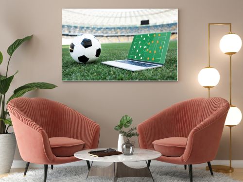 soccer ball and laptop with formation on screen on grassy football pitch at stadium