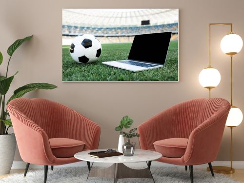 soccer ball and laptop with blank screen on grassy football pitch at stadium