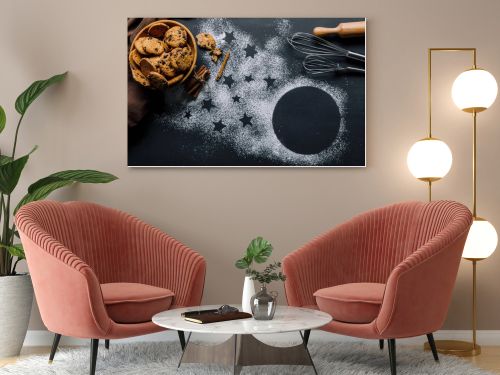 view from above of cookies in bowl, whisks and rolling pin on table covered by flour with symbol of stars