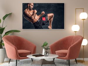 Profesjonalny bokser Muay Thai pokazujący technikę walki kopnięciami Zdjęcie studyjne na tle ciemnej ściany z teksturą