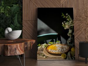 Freshly baked homemade lemon pie with floral crust decorations  in baking form, lemons and cherry blossom  on old wooden table on dark background. 