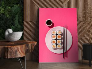 Japanese Sushi roll with salmon, cucumber and soy sauce with chopsticks in the plate on pink background with hard shadow. Concept food photography. Top view and copy space