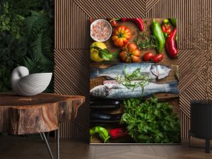 Raw uncooked seabass fish with vegetables, grains, herbs and spices on chopping board over rustic wooden background