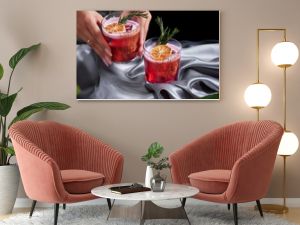 Red drink cocktail of rum and mezcal with lime and cherry juice garnished with dried fruit and green rosemary placed by two female hands