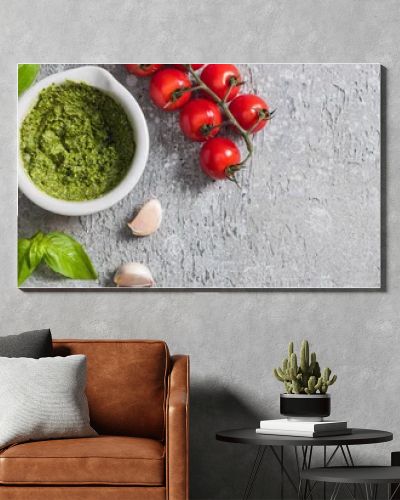 top view of raw tomatoes, garlic, basil, pine nuts, olive oil, pesto sauce on grey surface, panoramic shot