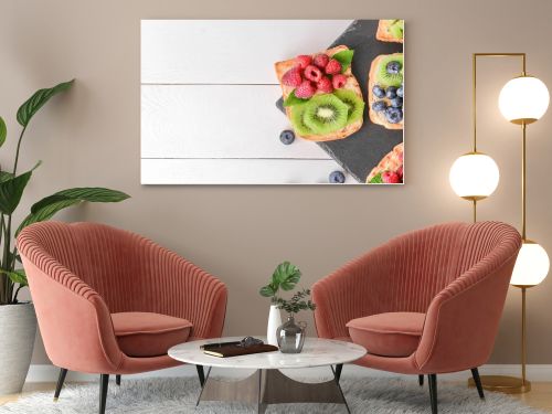 Slate plate with tasty sandwiches, kiwi and berries on white table