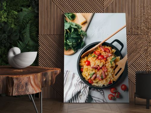 elevated view of pasta with jamon, cherry tomatoes, mint leaves covered by grated parmesan in pan with wooden spatula and spoon on marble table