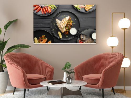 Top view of various grilled dishes served on a dark table in a restaurant. Fish fillet with vegetables. Flat lay