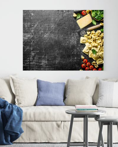 An assortment of different types of raw pasta with cheese, tomatoes and herbs. On dark rustic background