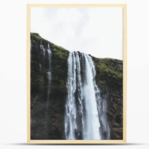 low angle view of Seljalandsfoss waterfall in highlands under cloudy sky in Iceland 