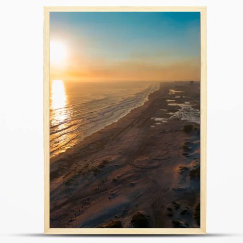 Cinematic 4K aerial drone footage captures Miramar Beach dunes at sunrise in Ciudad Madero, Tamaulipas. Warm orange and golden light paints the sky and reflects on the calm sea as the coastline stretches to the horizon. Palapas line the shore while A