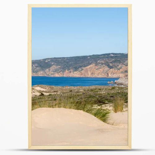 Sandy dune landscape with a wooden coastal path and distant rocky cliffs along the Atlantic coast near Guincho Cascais Portugal.