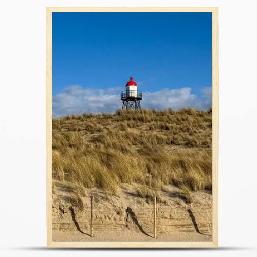 Scenic Dutch dune landscape featuring sandy hills, dry grass and a red and white lighthouse beneath bright clouds and blue sky. Peaceful coastal nature scene suitable for travel, tourism and environmental concepts.