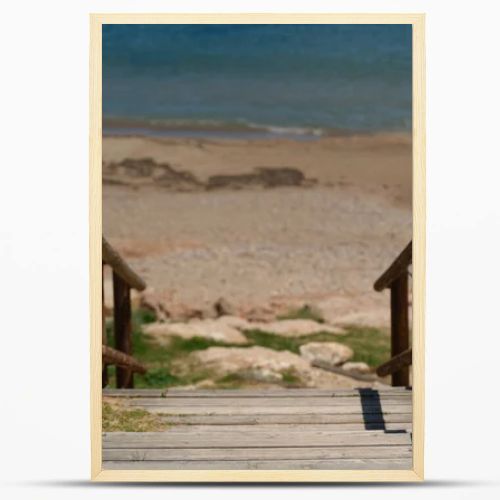 Wooden boardwalk with railings leading to a quiet sandy beach and turquoise Mediterranean sea. Sunny coastal scene with clear blue sky and peaceful vacation atmosphere.