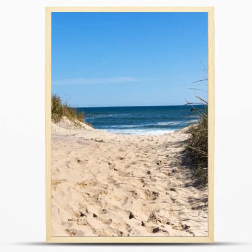 View of the Atlantic Ocean looking through a sand dune at Montauk Beach with footprints in the center and beach grass on the sides.