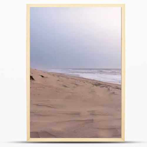 A serene, sandy beach with gentle waves against the shore under a soft, pastel sky. Dunes with sparse vegetation rise gently from the beach, creating a peaceful and untouched natural landscape.