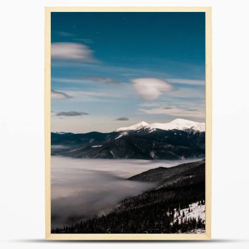 scenic view of snowy mountains with pine trees and white fluffy clouds in dark sky in evening