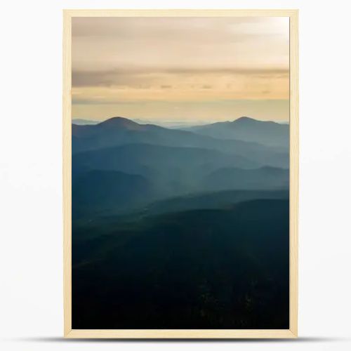 Aerial view of dark mountain hills with bright sunrays of setting sun at sunset. Hazy peaks and misty valleys in evening.