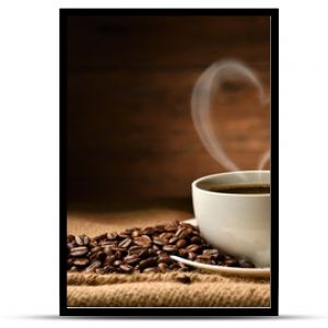 Filiżanka kawy z dymem w kształcie serca i ziarnami kawy na worku jutowym na starym drewnianym tle