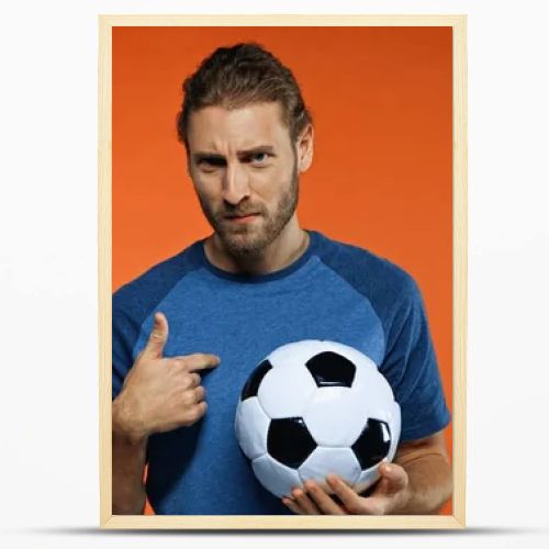 football fan in blue t-shirt holding soccer ball and pointing at himself on orange 