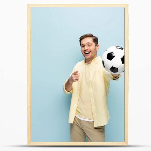 happy man in yellow shirt pointing with finger and holding football on blue