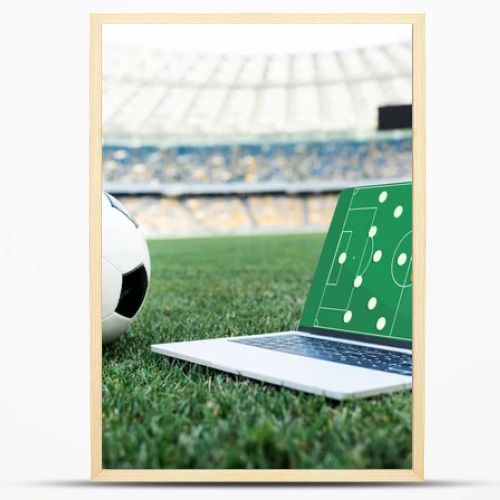 soccer ball and laptop with formation on screen on grassy football pitch at stadium