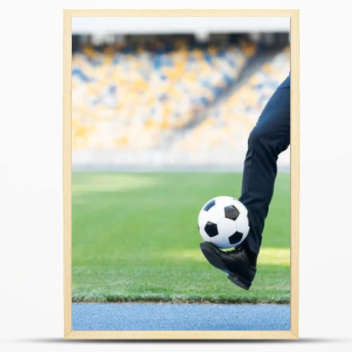 cropped view of young businessman in suit playing with soccer ball at stadium