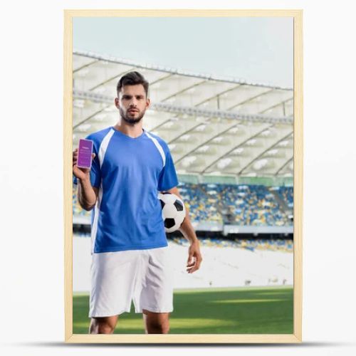 KYIV, UKRAINE - JUNE 20, 2019: professional soccer player in blue and white uniform with ball showing smartphone with Instagram app at stadium