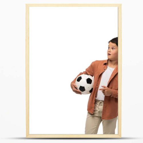 shocked boy holding soccer ball, looking away and pointing with finger isolated on white