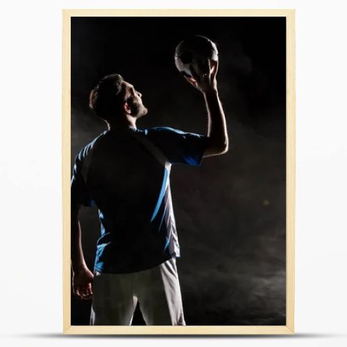 silhouette of player in uniform holding ball above head on black with smoke  