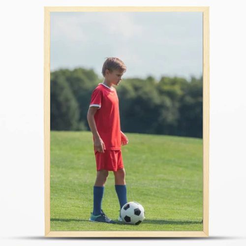 cute curly boy playing football with friend on grass in park 