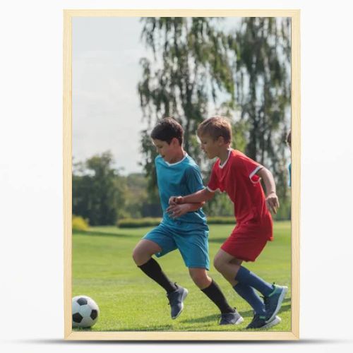 four multicultural kids playing football on grass  