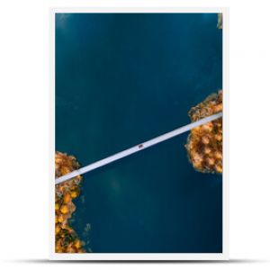 Aerial view of bridge road with red car over blue water lake or sea with island and autumn color woods in Finland.